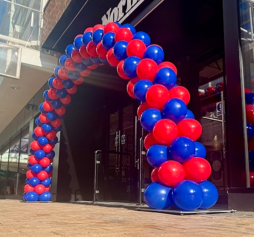 A colorful archway made of alternating red and blue balloons stands at the entrance of a storefront.